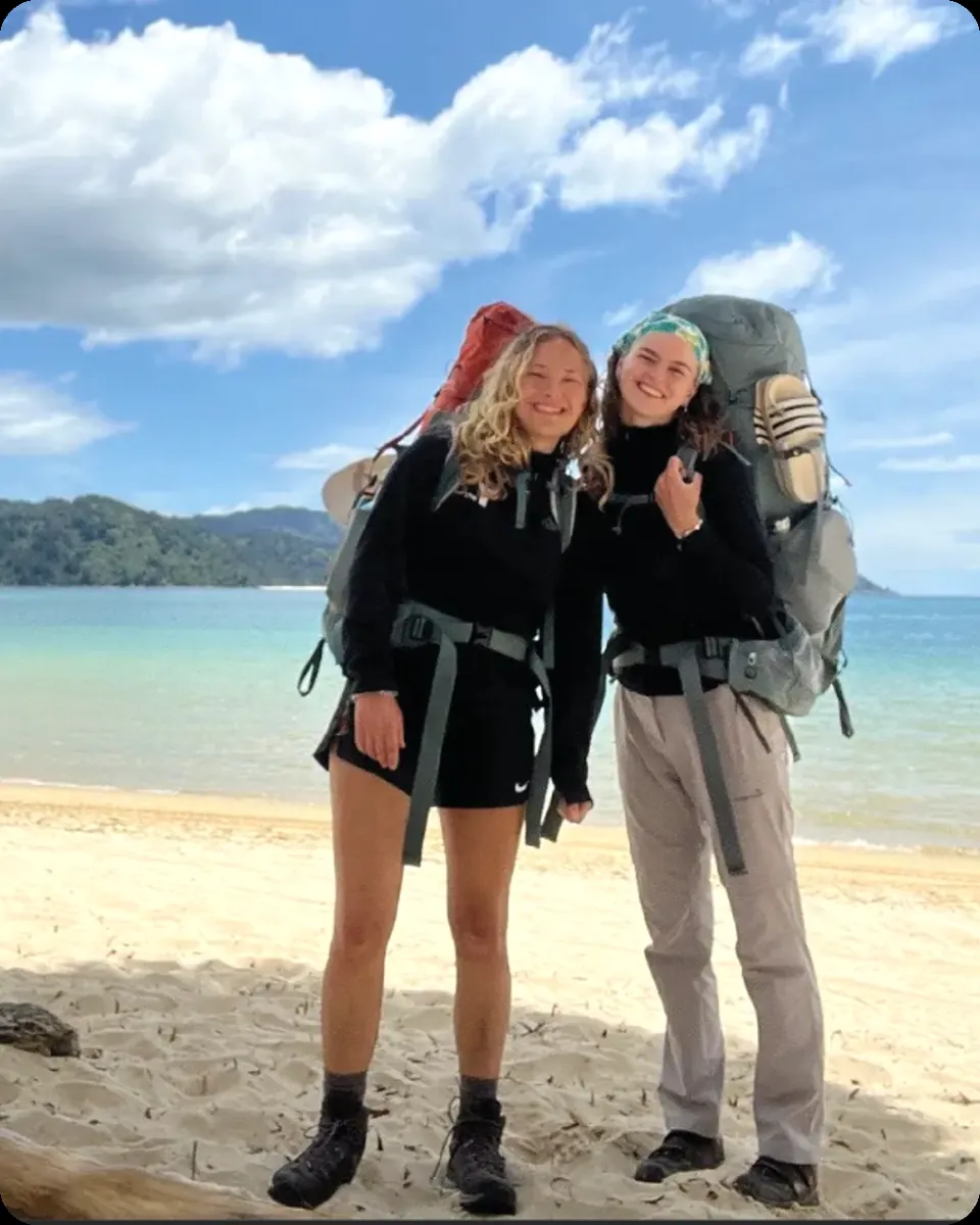 Dos participantes con mochila en una playa de Nueva Zelanda